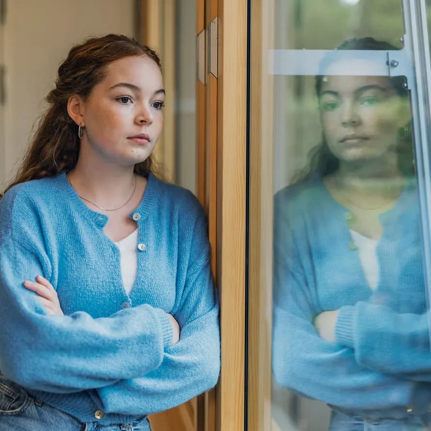 79646_SOS-KD_JuMa_Campus_MareenFischinger_20220904_SOS_J-1_8829a.jpg Jugendliche in blauer Strickjacke blickt nachdenklich aus dem Fenster.