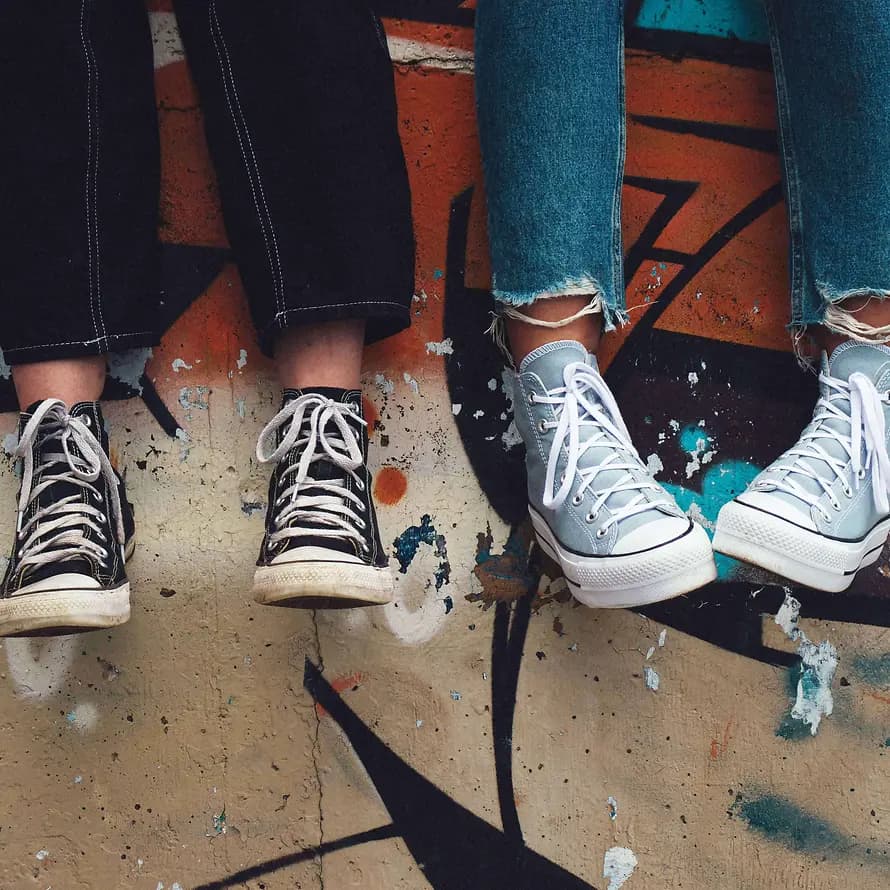 zwei Jugendliche mit Sneakers lassen die Füße vor einer Graffiti-Wand baumeln
