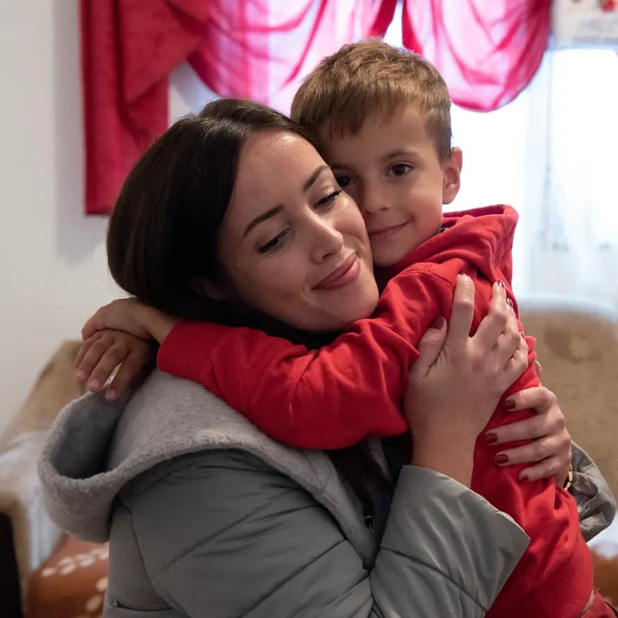Die Wärmepumpen erhöhen die Sicherheit der Kinder. Junge Frau umarmt Kind in Wohnzimmer.