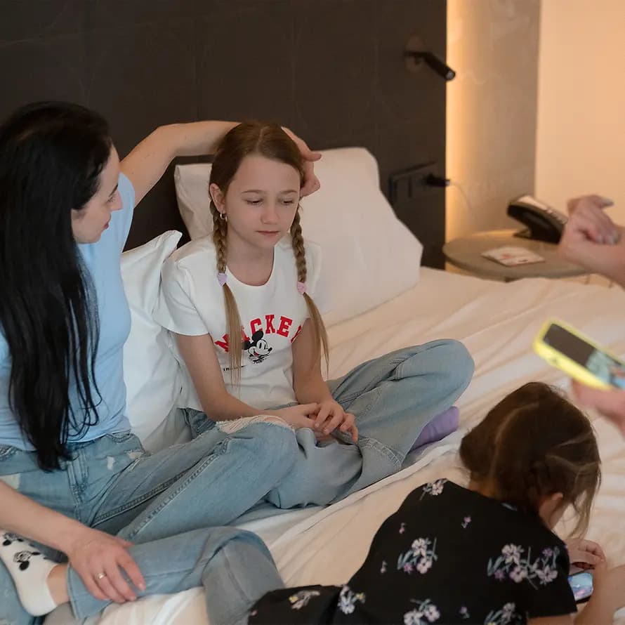 Mädchen sitzen in einem Hotelzimmer auf dem Bett, während eine Frau neben ihnen telefoniert