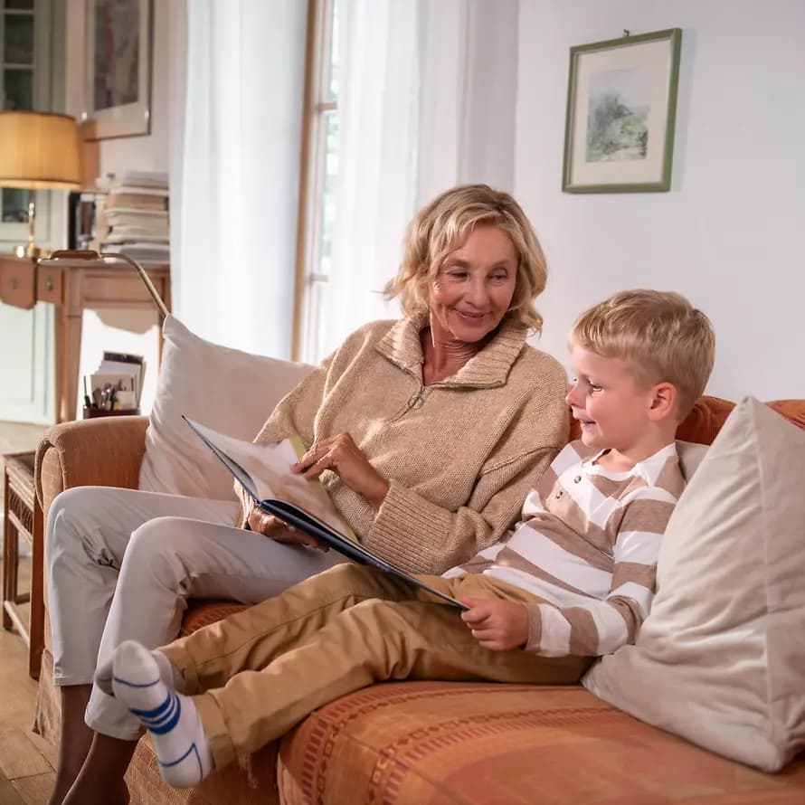 90393_Erbschaftsmarketing_Imagefilm_10-0-Bilderbuch-Couch-4574_sRGB.jpg Oma und Enkel schauen gemeinsam Bilderbuch auf Couch an