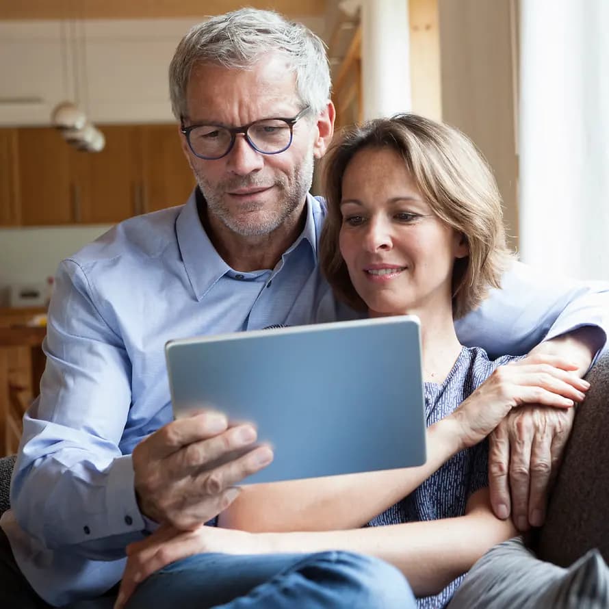 98033_SOS-KD_Westend61_RainerBerg_RBF004892.jpg Paar mittleren Alters sitzt auf Sofa und schaut gemeinsam auf Tablet