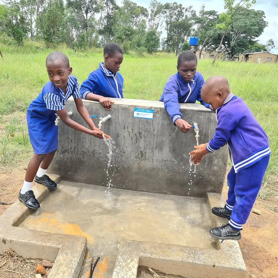 98607_SOS-Kinderdorf Simbabwe_3_Hwedza_Grundschule_Wasser (5).jpg Kinder in Schuluniformen in Simbabwe waschen Hände an Wasserhähnen im Freien