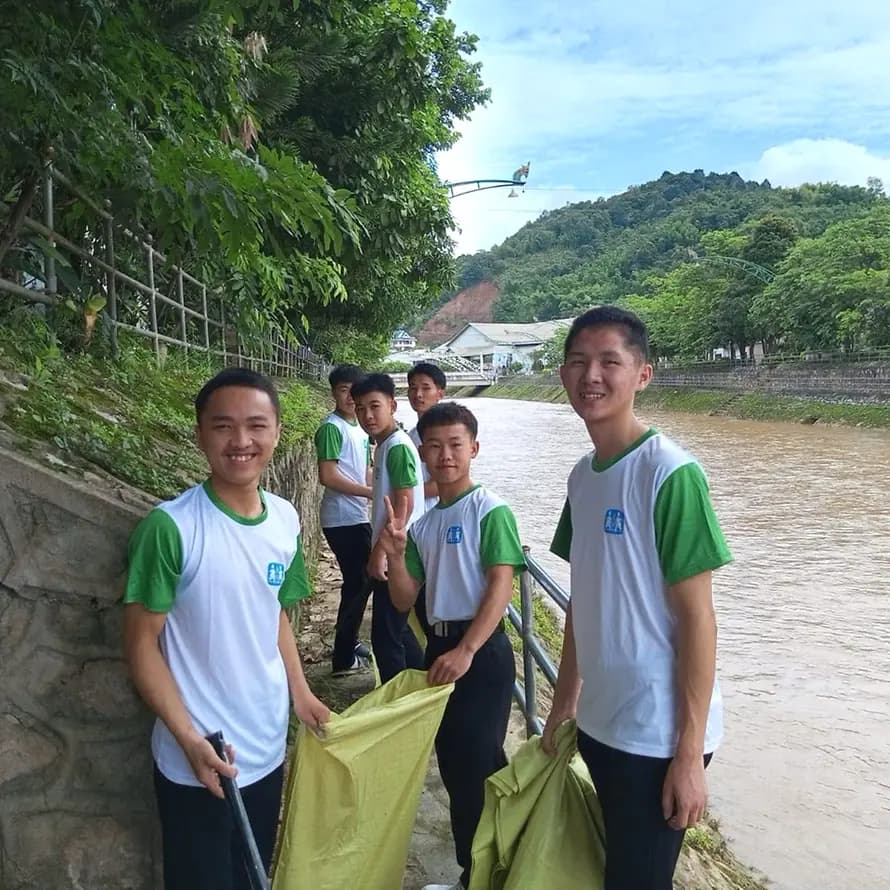 98622_SOS-Kinderdorf Laos_Sam Neua_4 (3).jpeg Jugendliche mit SOS-Kinderdorf-T-Shirts und Müllsäcken in den Händen stehen an Flussufer