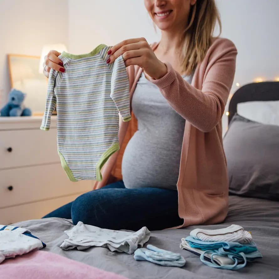 Babygrundausstattung Babygrundausstattung - Frau betrachtet lächeln einen Babystrampler