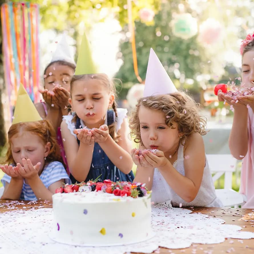 99801_SOS-KD_Westend61_inimages_HPIF17648.jpg Kinder mit Geburtstagshütchen stehen vor Torte und pusten Konfetti