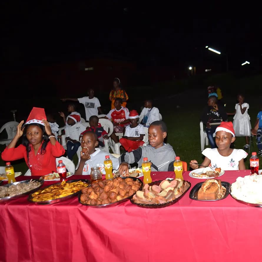 123059_SOS-Kinderdorf Kamerun_Weihnachten (6).JPG Kinder im SOS-KInderdorf sitzen draußen an langem Tisch mit vielen Platten voller Essen