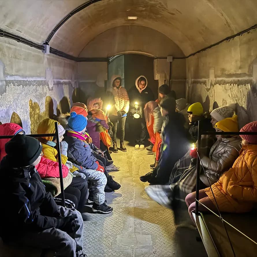 123992_SOS-Kinderdorf Ukraine_Kinder im Bunker in Brovary.jpg Kinder und Betreuerinnen in dicken Jacken mit Taschenlampen im Bunker