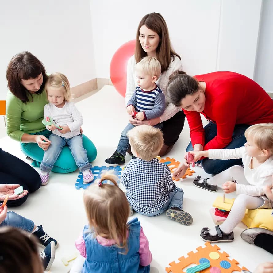 45502_shutterstock_1035292636_OksanaShufrych.jpg Mehrere Frauen sitzen mit kleineren Kindern am Boden im Kreis und spielen gemeinsam