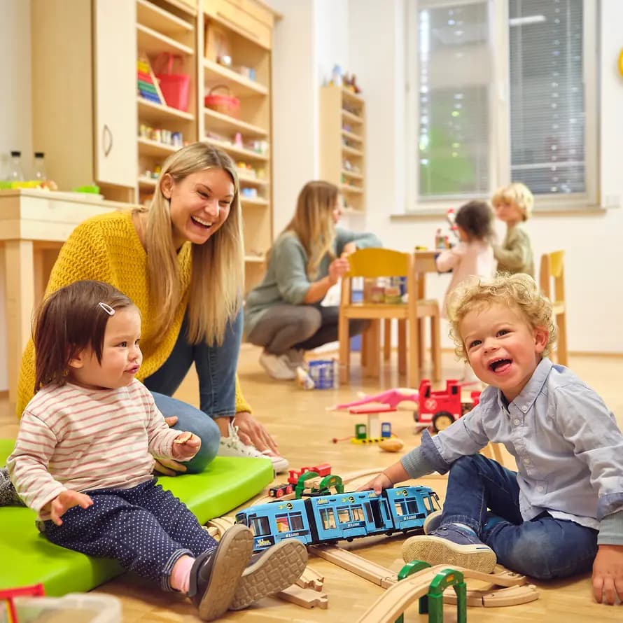 70843_SOS-KD_München_BergamLaim_ER-Modell-Shooting_25092021_AndreKirsch_7733.jpg Eine Frau spielt mit zwei kleinen Kindern am Boden mit Spielzeug