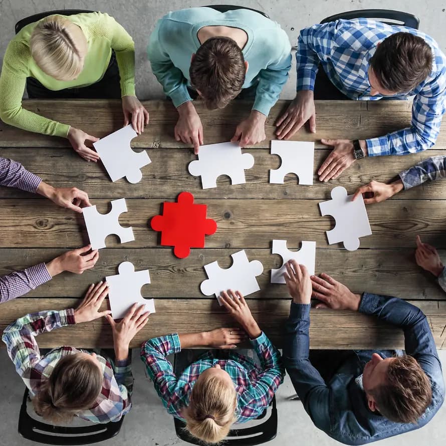 72058_SOS-KD_shutterstock_ALot OfPeople_1089781793.jpg Menschen sitzen am Tisch mit großen Puzzleteilen aus der Vogelperspektive