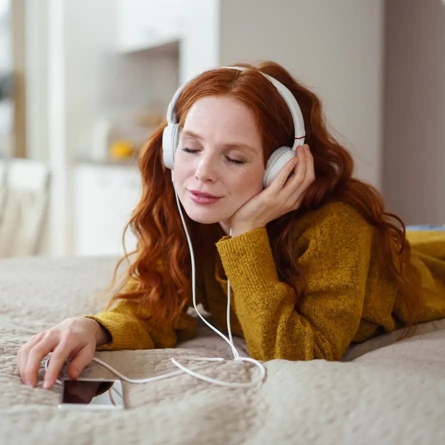 Musik, Podcast und mehr hören Frau die auf dem Bett mit dem Handy Musik/Podcast hört