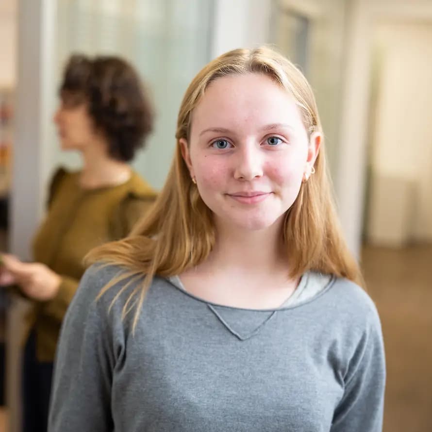 Care Leaver SOS-Kinderdorf Mädchen mit blonden Haaren im Vordergrund, im Hintergrund zwei Frauen, die sich unterhalten