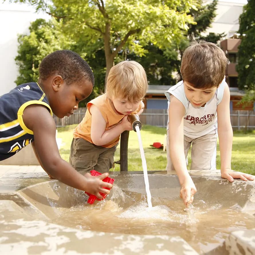 Draußen spielen und Freunde treffen Drei Kinder spielen im Freien mit Wasser