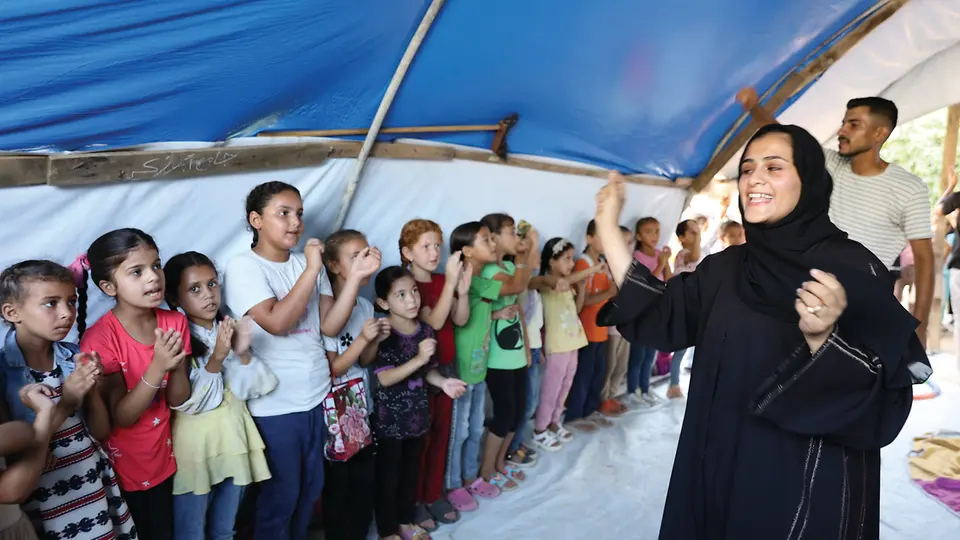 Kinder stehen in einer Reihe in Zelt im SOS-Camp in Gaza und klatschen, Betreuerin macht es vor.